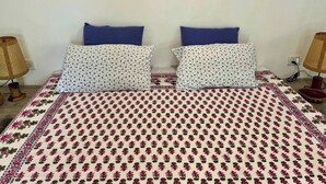 Cama com roupa de cama estampada com flores, duas almofadas com desenho de pássaros e duas luminárias de cada lado.