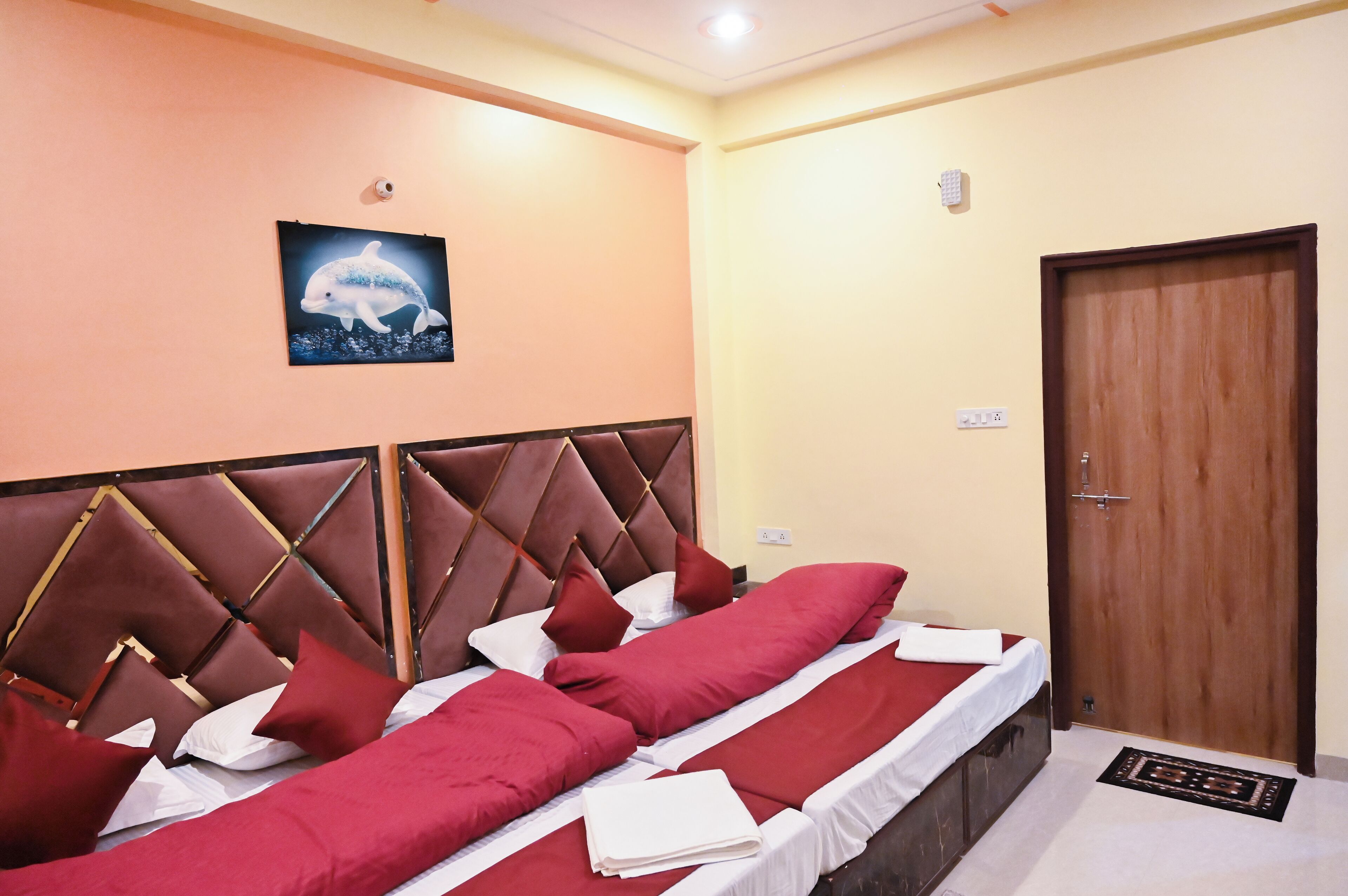 A hotel room with two beds, a wooden door, and a dolphin artwork on the wall.