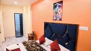 A hotel room with a bed, a painting on the wall, and a door leading to another room. - Amaya Deluxe (Varanasi)