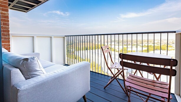 A balcony with a sofa and a wooden bench, overlooking a cityscape. - Luxury Apt Near Canary Wharf (Greater London)