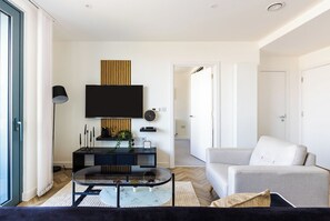 A modern living room with a sofa, coffee table, TV, and a console table with decorative items. - Luxury Apt Near Canary Wharf (Greater London)