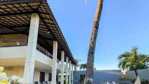 Un resort con zona de piscina, palmeras y un porche cubierto.