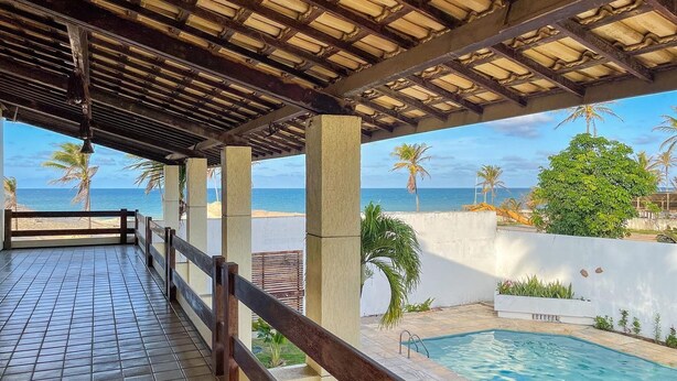 Un espacio al aire libre techado con piscina, vista a la playa y palmeras.