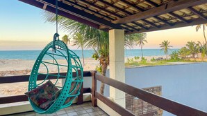 Un balcón con una hamaca colgante, vista a la playa y palmeras.