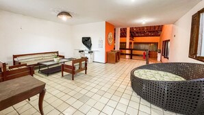Amplia sala de estar con una gran mesa redonda, un sofá y una mesa de centro. Se ve una escalera que conduce a un nivel superior con balcón.