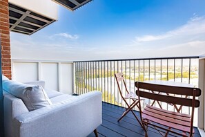 Ein Balkon mit einer Couch und einer Holzbank, mit Blick auf eine Stadtlandschaft.