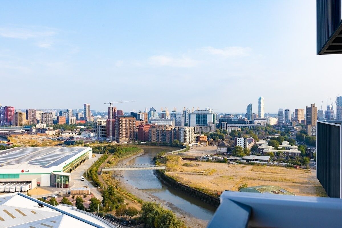 A cityscape with a river, modern buildings, and a large structure with a green roof.
