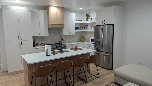 A modern kitchen with white cabinetry, a stainless steel refrigerator, a central island with bar stools, and a wooden ceiling. - Newly constructed, charming, ski-on ski-off condo (Beaver)