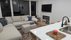 A modern living room with a sofa, ottomans, a coffee table, and a kitchen area with a sink and countertop. - Newly constructed, charming, ski-on ski-off condo (Beaver)