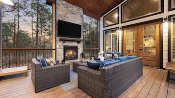 Une terrasse extérieure aménagée avec des meubles en osier, une cheminée en pierre et un téléviseur fixé au mur.
