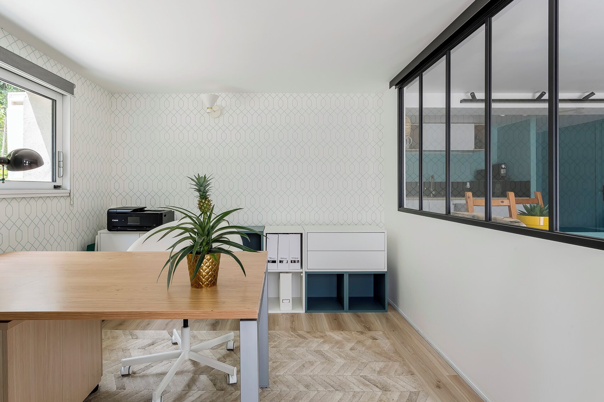 Een ruimtelijk kantoortje met een houten bureau, een witte stoel, een potplant en een printer.