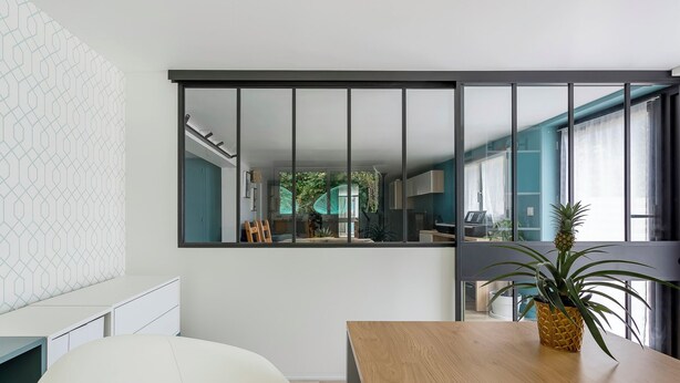 Un interior moderno con una mesa de comedor de madera, una silla blanca y un espejo grande que refleja una cocina con mesa y sillas.