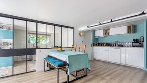 Una cocina moderna con armarios blancos, salpicadero verde azulado y una zona de comedor con banco y mesa.