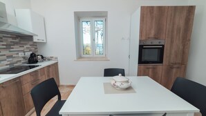 Een kleine keuken met een witte tafel, zwarte stoelen, een raam en een inbouwoven.