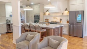 Une cuisine moderne avec des meubles blancs, un îlot central doté de tabourets et un réfrigérateur en acier inoxydable.