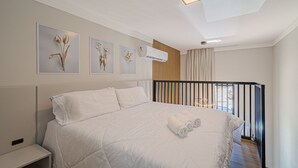 Een net opgemaakt bed met witte lakens, een nachtkastje en drie bloemachtige kunstwerken aan de muur.
