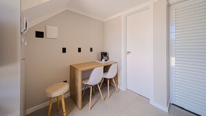 Een kleine, nette kamer met een houten bureau, twee witte stoelen, een koffiezetapparaat en een telefoon.