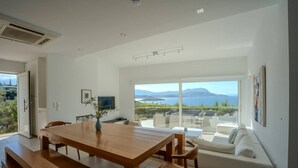 A modern dining area with a wooden table and benches, a sofa, and a TV on the wall.