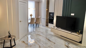 A modern living room with a marble floor, a flat-screen TV, a dining area with chairs, and a small table with a decorative item. - Premium Central Apartment • Eminescu Residence (Chișinău)