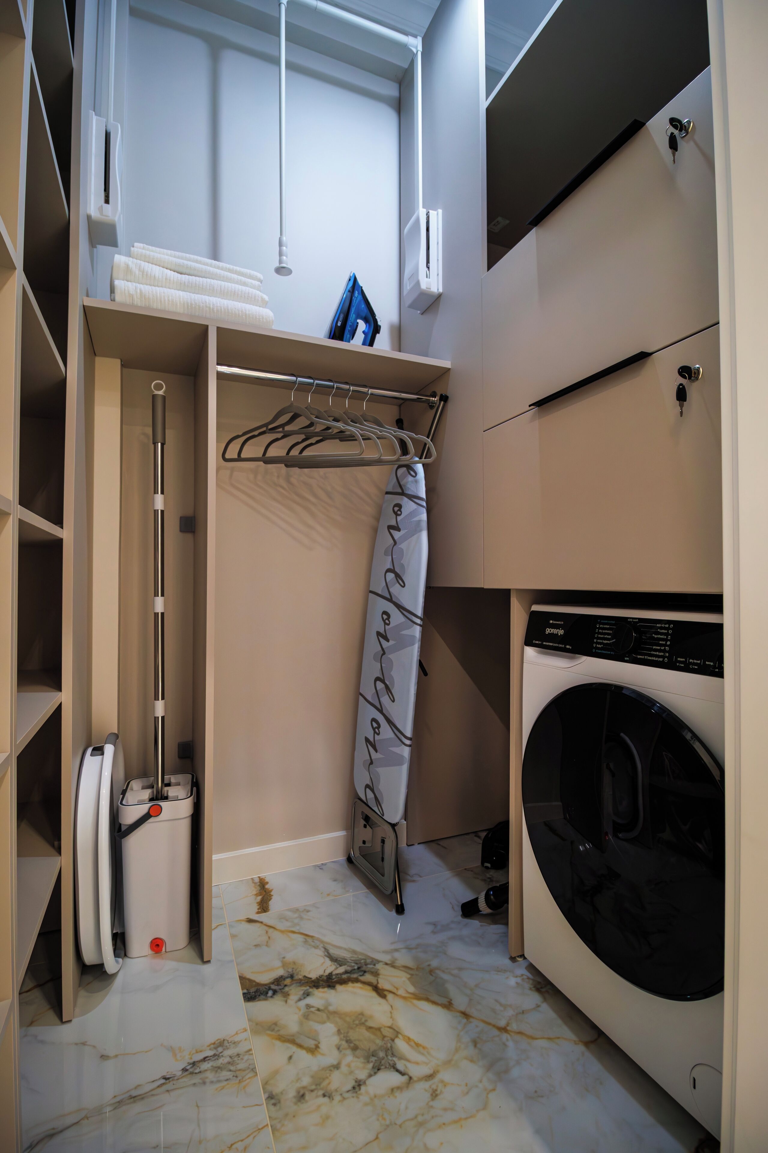 A compact laundry room with a washing machine, a drying rack, and a towel rack.