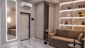 A modern living room with a marble floor, a beige sofa, a small round table, and a wall-mounted shelf with decorative items. - Premium Central Apartment • Eminescu Residence (Chișinău)