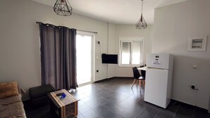 Un salon moderne comprenant un canapé, une petite table, un téléviseur et un coin cuisine avec un réfrigérateur.