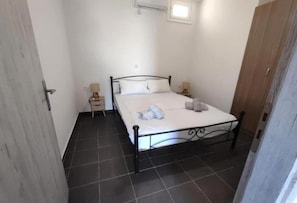 A small, clean room with a bed, two bedside tables, and a window. - Aegean Beachfront Apartment 2 (Klimaki)