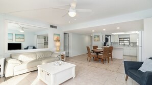 A spacious living room with a white sofa, a coffee table, and a dining area with wicker chairs. - Upscale Unit with 2 King Beds-One Level-Pool Front- Steps to Sand Beach & Pier! (Cocoa Beach)