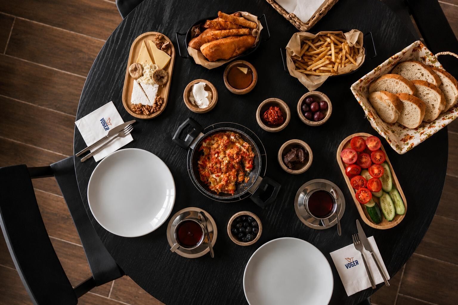 Una mesa redonda para comer con diferentes alimentos y utensilios, incluyendo platos, cuencos y una cesta de pan.