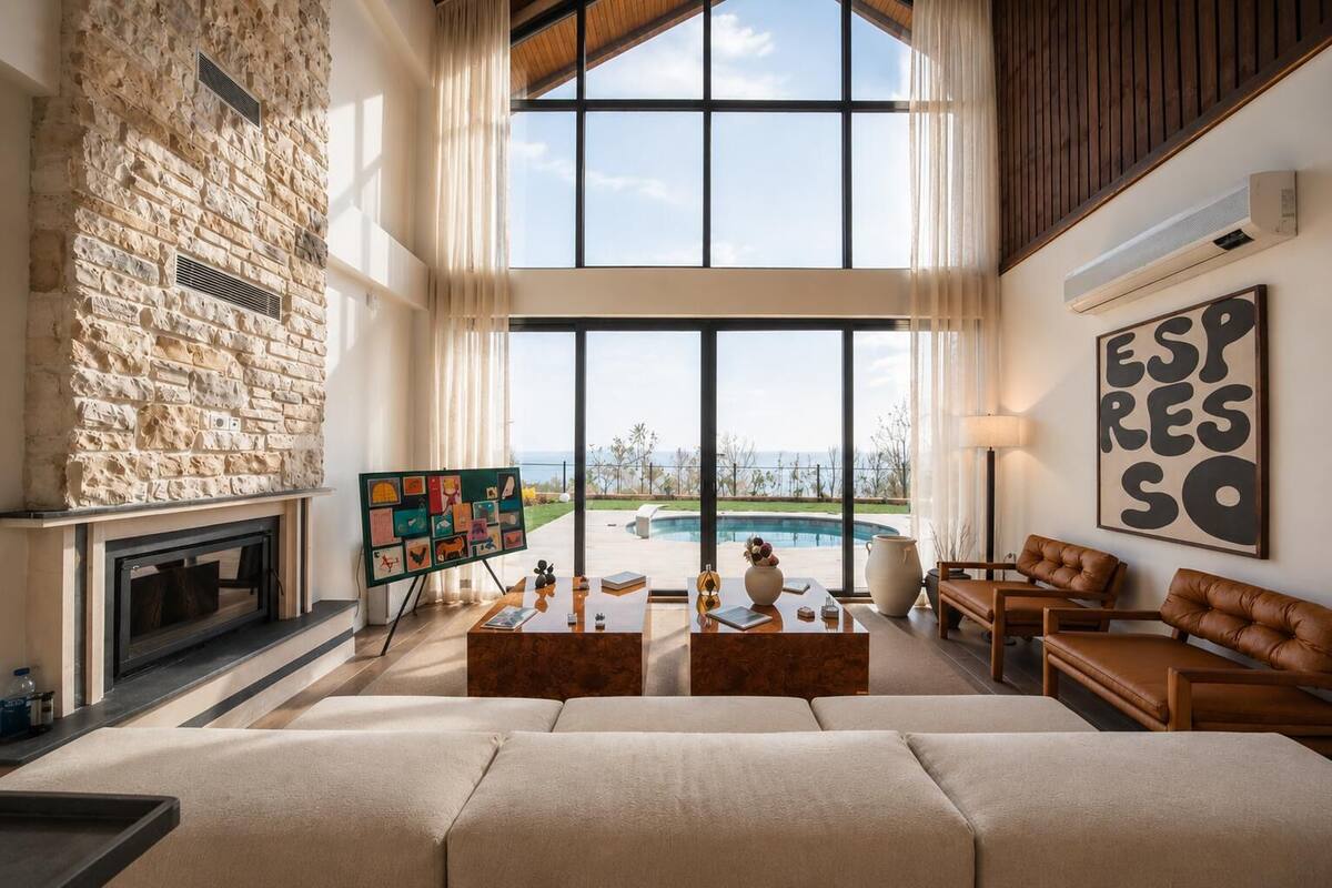 A spacious living room with a stone fireplace, large windows, a pool view, and a cozy seating area.