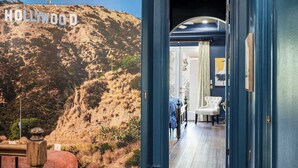 A hallway with a view of the Hollywood sign, a white chair, and a door leading to a room with a bed and curtains. - Hollywood Glam Villa w/ AGT Stage Arcade Pool Spa! (Kissimmee)
