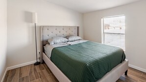 Een slaapkamer met een bed, een bedlampje en een raam met jaloezieën.