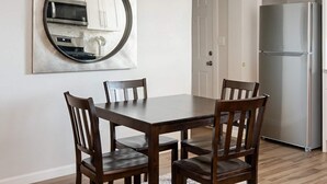 Een eetruimte met een houten tafel en stoelen, een grote spiegel aan de muur, en een keuken met een koelkast op de achtergrond.