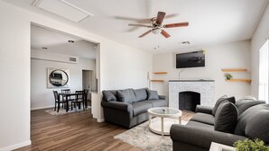 Een moderne woonkamer met een open haard, een plafondventilator en een flatscreen televisie erboven.