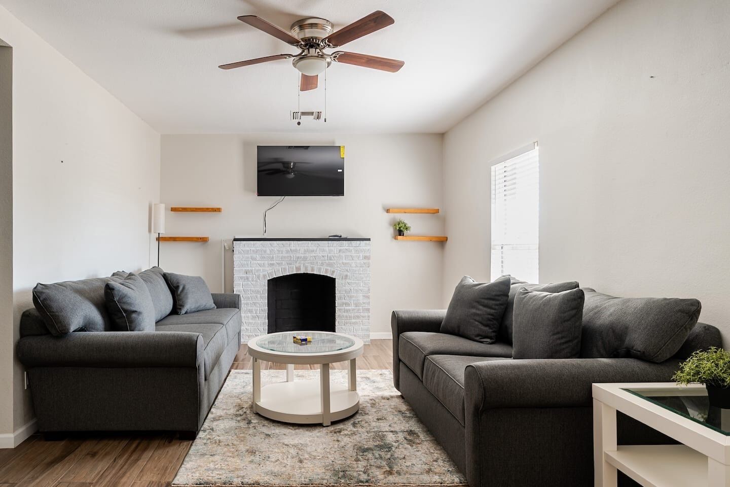 A modern living room with two grey sofas, a round coffee table, a fireplace, and a ceiling fan.