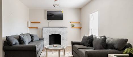 A modern living room with two grey sofas, a round coffee table, a fireplace, and a ceiling fan.
