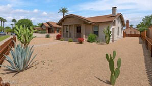 Een woonhuis met een grindpad, een houten hek en cactussen.