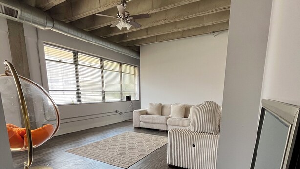 Un amplio salón con techo alto, un sillón colgante, un sofá y un ventanal con persianas.