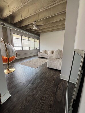 Un amplio salón con techo alto, un sillón colgante, un sofá y un ventanal con persianas.