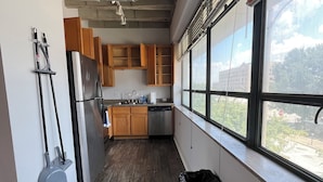 Una cocina con armarios de madera, un refrigerador de acero inoxidable y una ventana con vistas a edificios y árboles.
