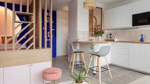 A modern kitchen with white cabinets, a black oven, and a wooden island. There are two bar stools and a pink ottoman. - Cosy 33m2 studio with view of Monts d'Or & Lyon (Dardilly)