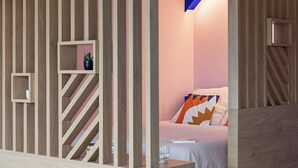 A modern room with a wooden slat partition, a bed with a colorful pillow, and a small shelf with a plant. - Cosy 33m2 studio with view of Monts d'Or & Lyon (Dardilly)