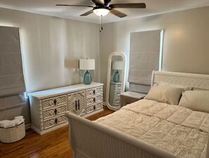 Ein Schlafzimmer mit Bett, Schminktisch, Nachttischen und Deckenventilator.