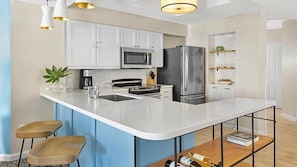 A modern kitchen with white cabinets, stainless steel appliances, a bar counter, and a seating area with stools.