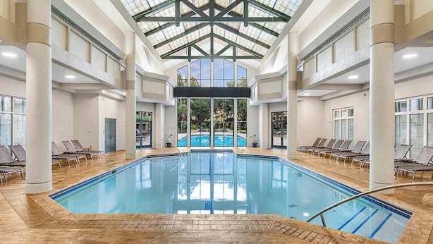 Une piscine intérieure dotée d’un toit en verre, entourée de chaises longues et offrant une vue sur l’extérieur.