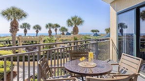 Un balcon avec une table et des chaises, des palmiers et une vue sur la plage.