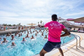 A swimming pool area with multiple people in the water, a person in a pink shirt, and a water slide in the background. - KLASSIK 2-Bedroom Mobile Home "DIMANCHE" - No Air Conditioning - Sleeps 5 (SERIGNAN)