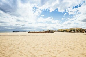 Ein weiter, sandiger Strand mit blauem Himmel und vereinzelten Wolken.