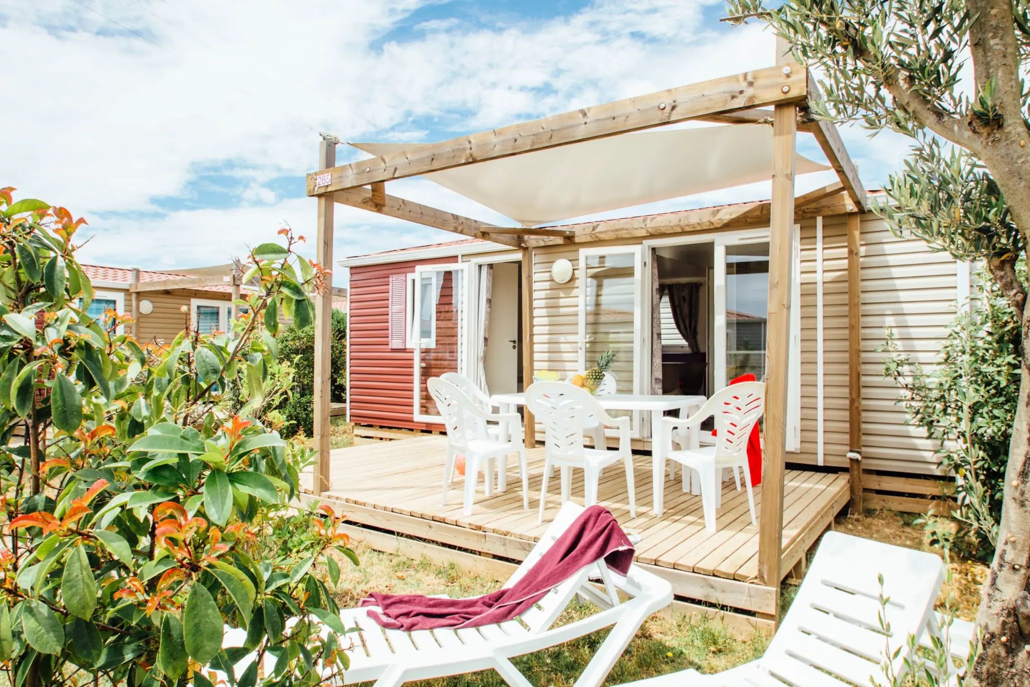 Une terrasse en bois avec des meubles d’extérieur, un espace salon couvert et une vue sur un bâtiment rouge.