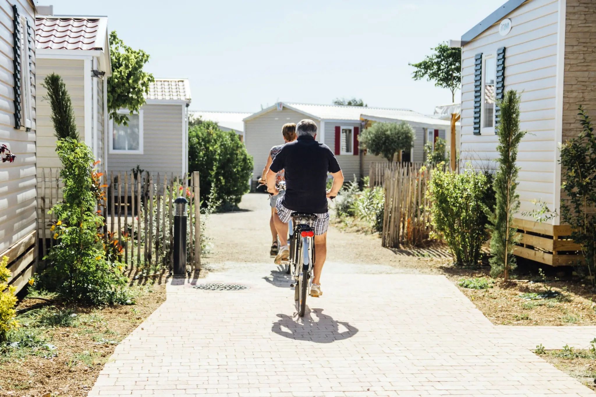 A pathway leading to a row of mobile homes with a wooden fence on one side and a garden area on the other.